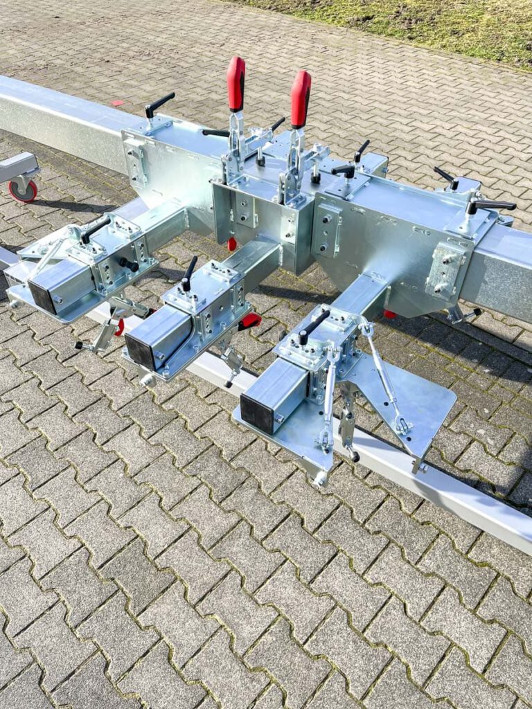 Detailaufnahme eines stabilen, galvanisierten Fahrgestells mit mehreren Bedienhebeln und Klemmen, geeignet für den Einsatz in der Fahrzeug- oder Maschinenmontage, auf einem gepflasterten Untergrund.